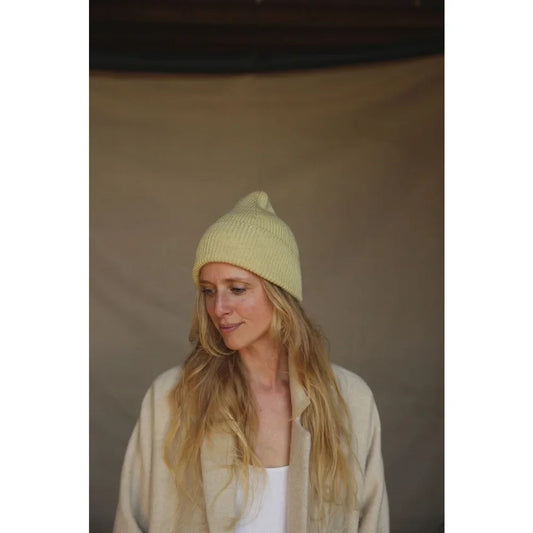 Frau mit blonden Haaren in cremefarbener Mütze und weißem Oberteil