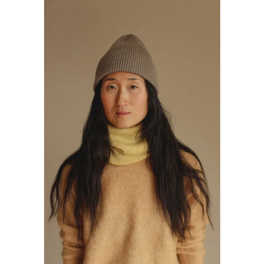 Frau mit langem dunklem Haar, Beanie, gelbem Rollkragen und beigem Pullover