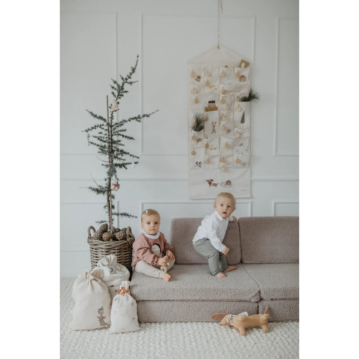 Zwei Kinder auf einem modularen Sofa mit Weihnachtsdeko und dem Adventskalender mit gestickten Illustrationen