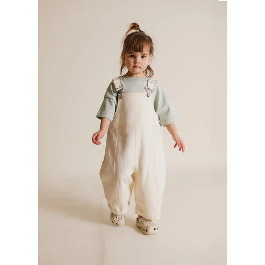 Kleinkind trägt weiße Latzhose und grünes Hemd im August Dungaree Ecru