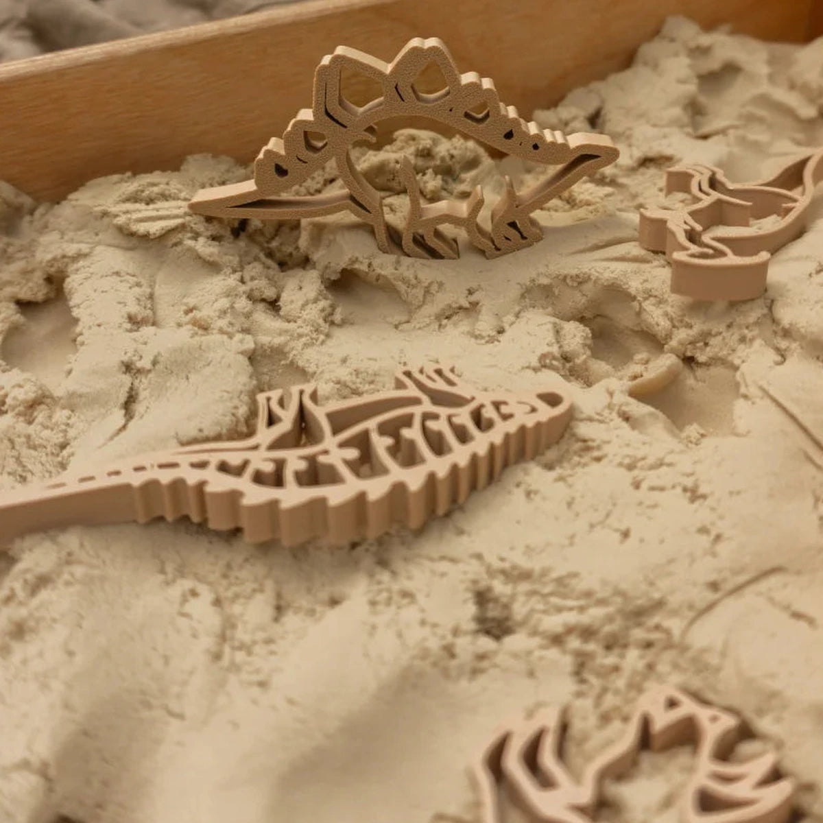 Puzzle scheletro di dinosauro in legno nella sabbia, plastica biodegradabile e formina dino verde