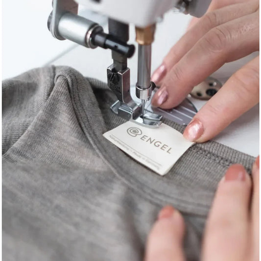 Sewing machine befestigt ein Etikett an grauem Stoff des Baby Body Langarm Walnuss