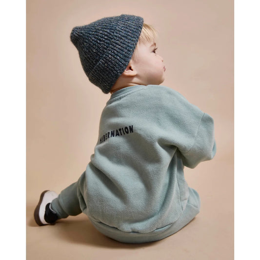 Baby in einem tealfarbenen Strickmütze und passendem Sweatshirt für die Baby Hibernation Kollektion