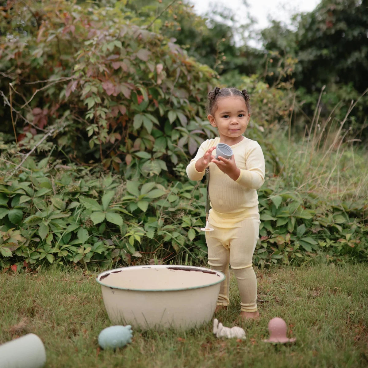 Junges Kind steht neben einer Schüssel mit bunten Eiern auf dem Boden