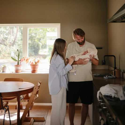 Ein Paar hält und betrachtet ein Neugeborenes in einer Küche mit Badetuch mit Kapuze