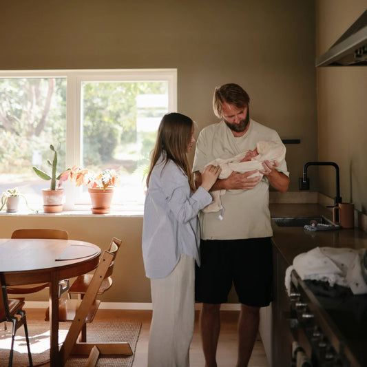 Ein Paar hält und betrachtet ein Neugeborenes in einer Küche mit Badetuch mit Kapuze