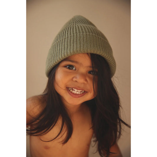 Lächelndes Kind trägt grüne Strickmütze Beanie Fonzie in Artischockenfarbe