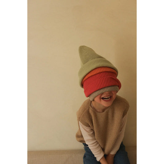 Jemand trägt gestapelte Wintermützen in Rot und Beige und lacht