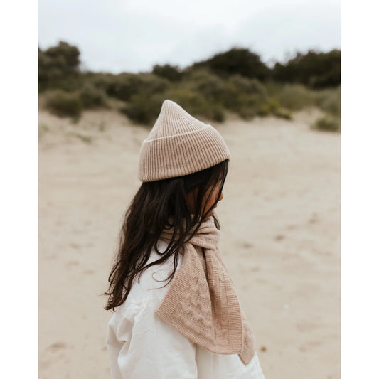 Person in Beanie Fonzie Sand and light clothing enjoying a sunny beach day