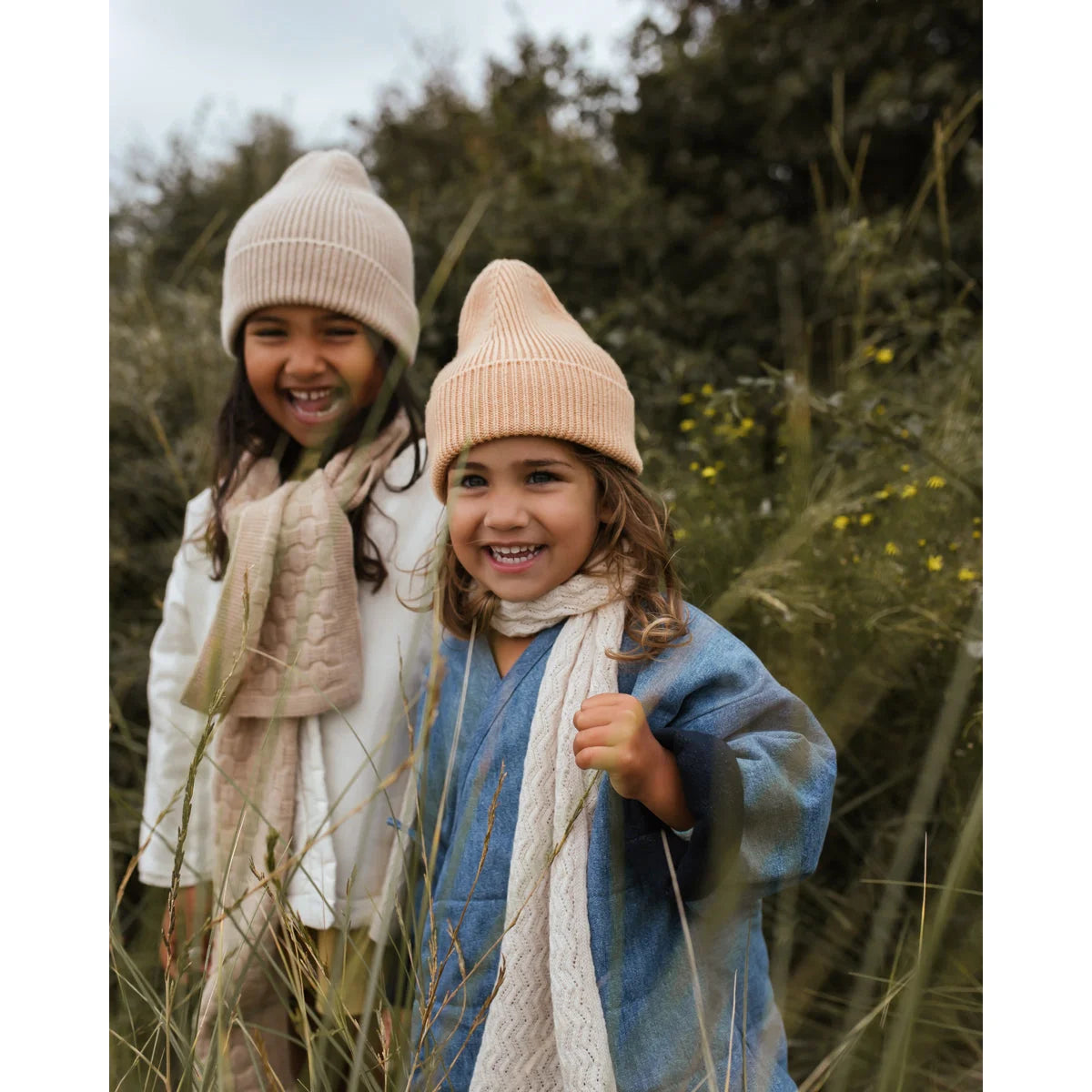 Zwei lächelnde Mädchen tragen Beanie Fonzie Sand und Schals im Freien