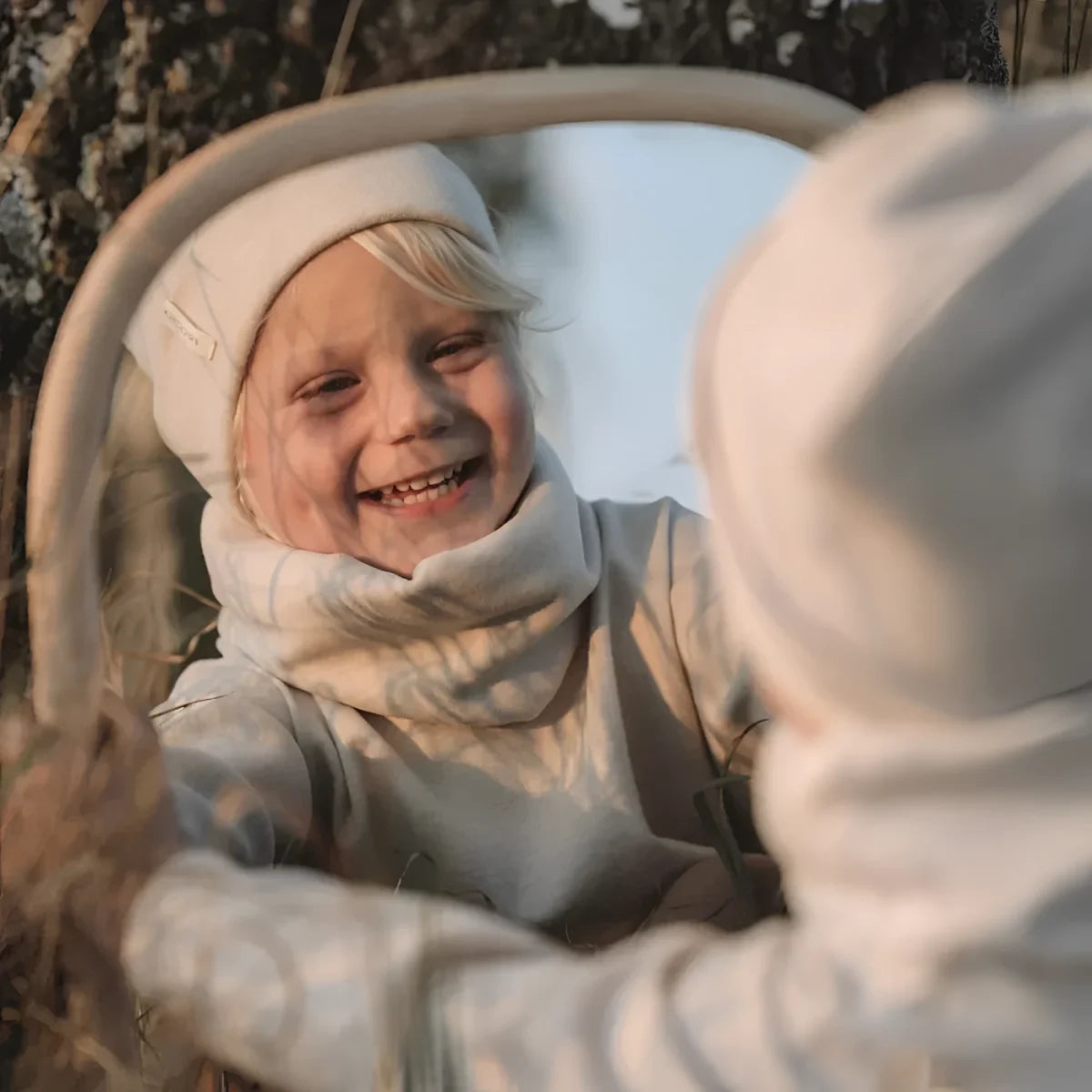Lächelndes Kind in Winterkleidung, reflektiert im Autospiegel mit Beanie rib strick beige