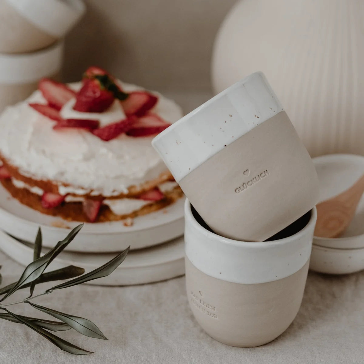 Zwei gestapelte Becher GLÜCKLICH 320ml in mattem Beige-Weiß mit Speckeln für bessere Tage