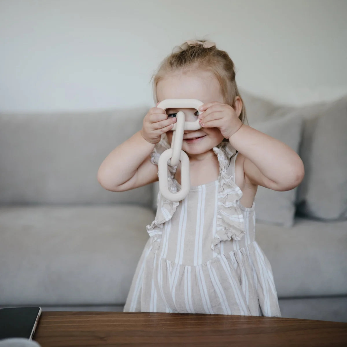 Junges Kind verdeckt die Augen mit einem Holzspielzeug in einem weißen Kleid