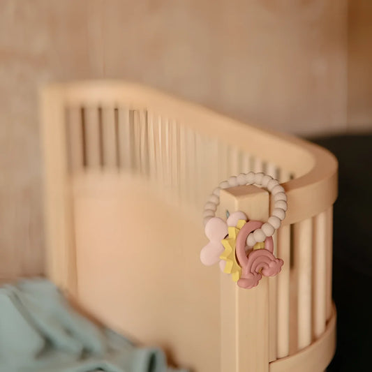 Pastellrosa und gelber silikon baby-beißring mit regenbogendesign an einem holzgitter befestigt beissring nature