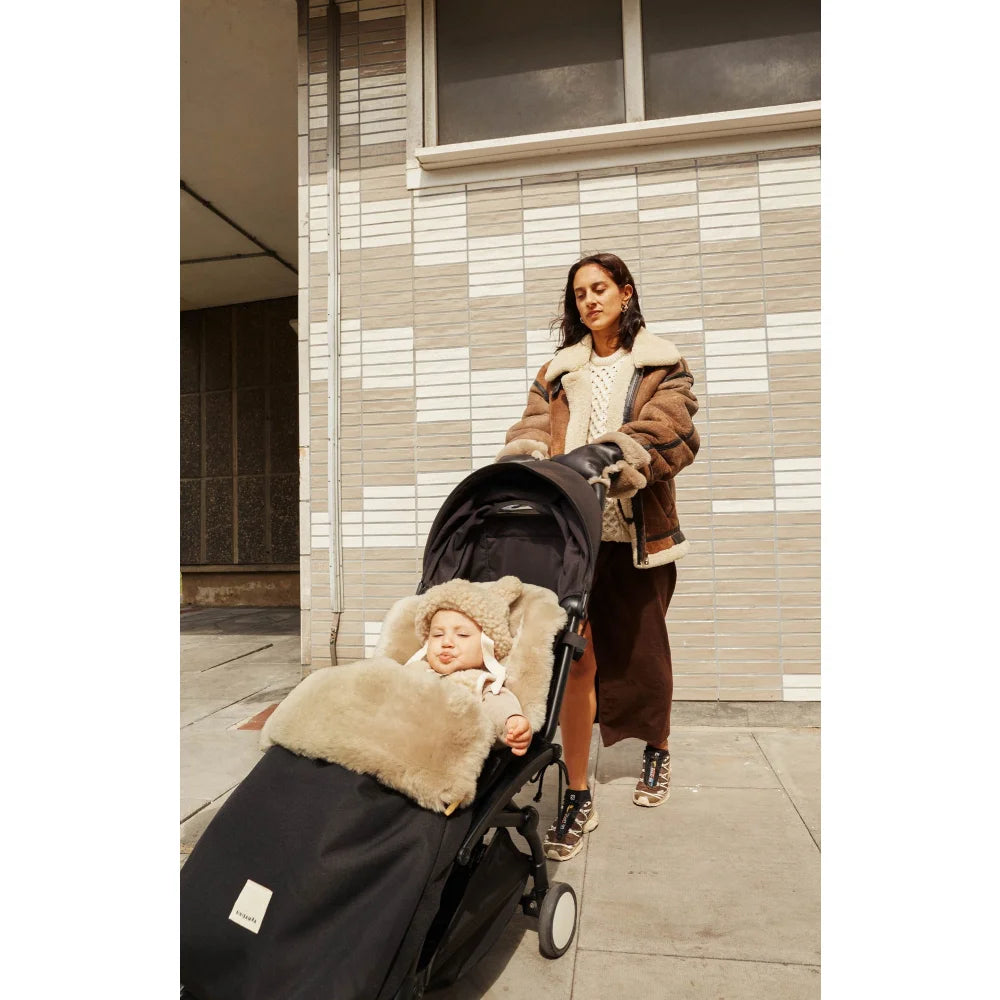 Frau schiebt Kinderwagen auf einem Bürgersteig mit beschichteten Handschuhen