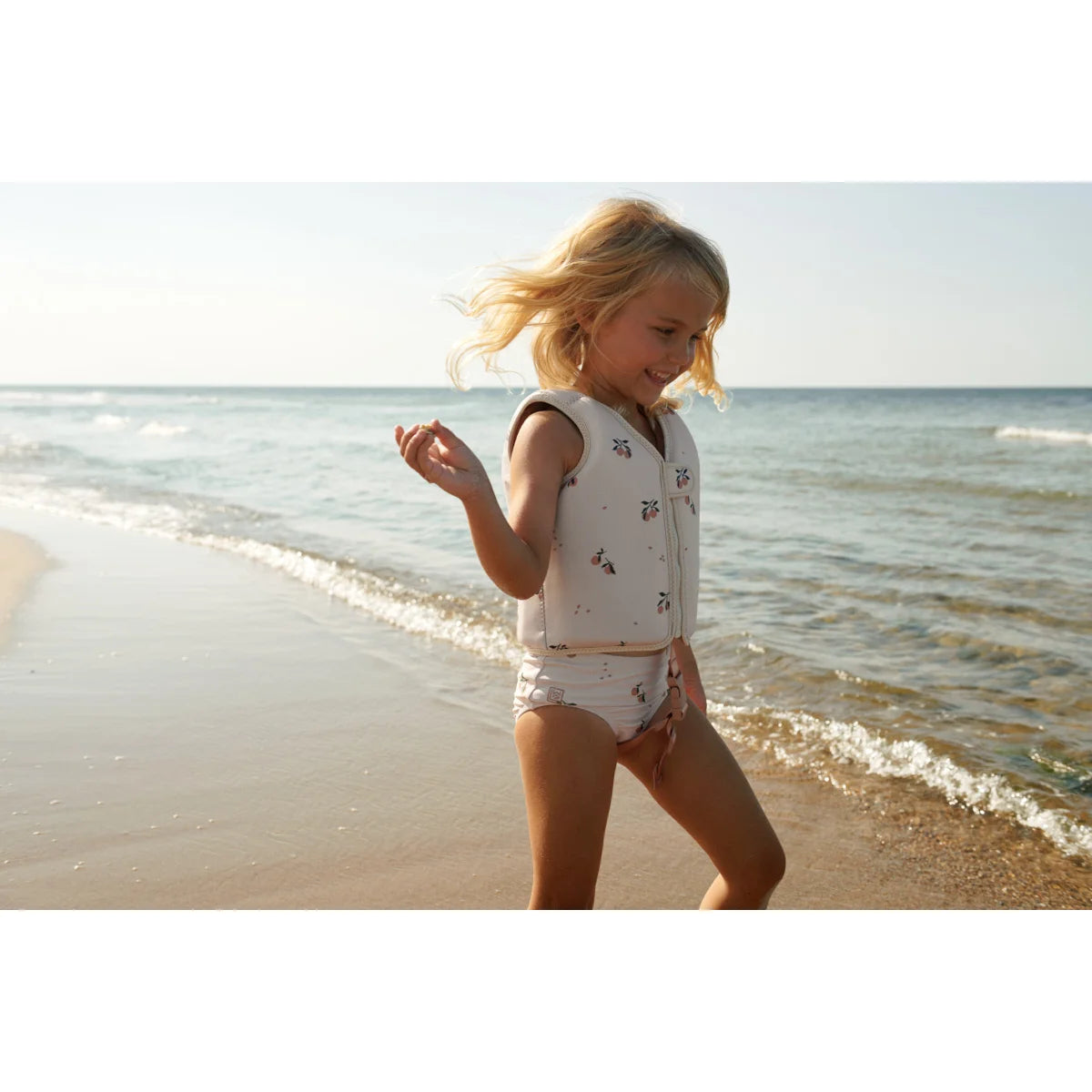 Kind spielt fröhlich am Strand in einem weißen gemusterten Badeanzug