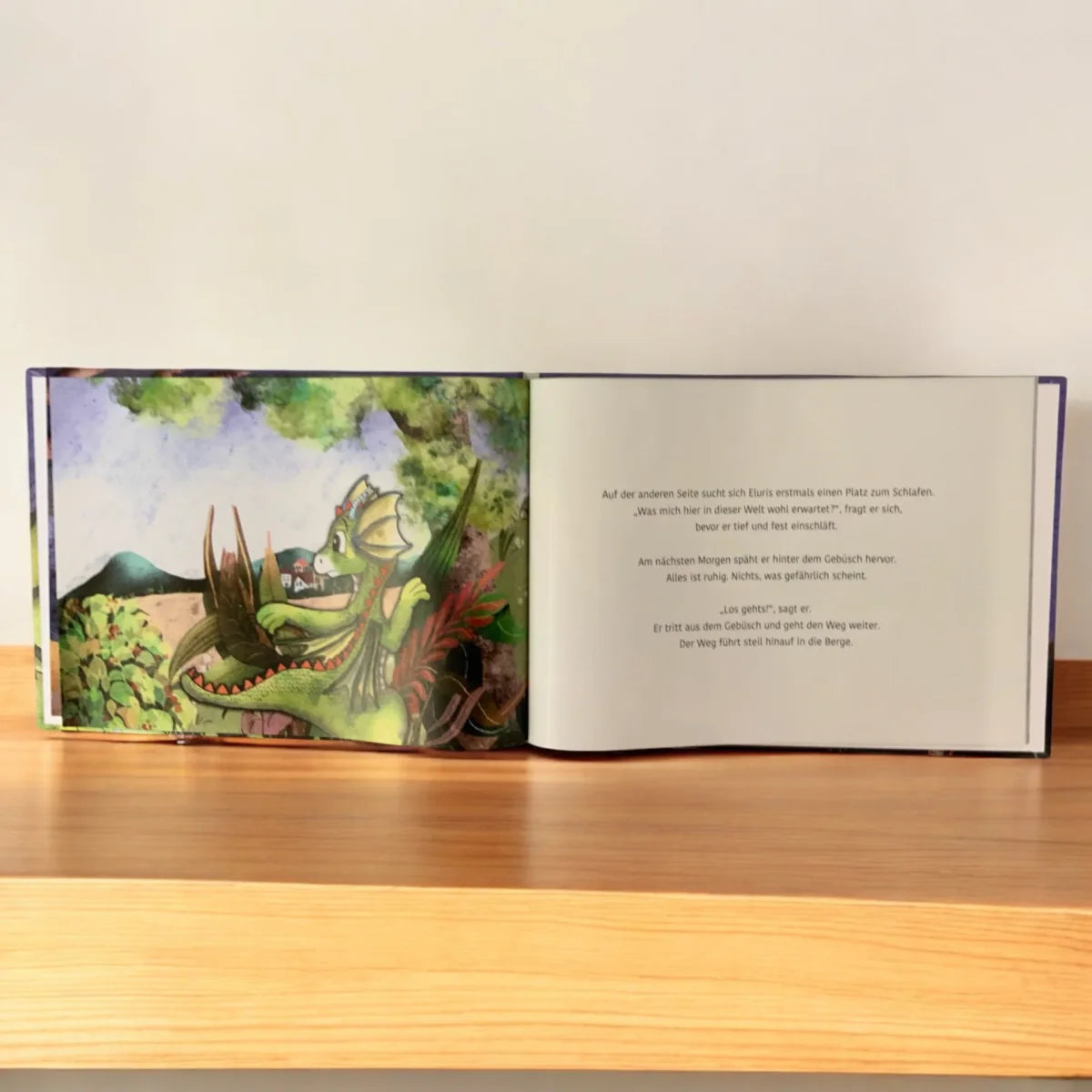 Offenes Kinderbuch mit farbenfroher Wasserfarbillustration eines Drachen in Eluris und der Kristall