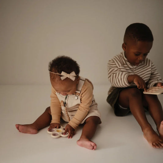 Zwei Kinder spielen mit Blume Plop-it Spielzeug in Lila und Gelb, einer liest ein Buch