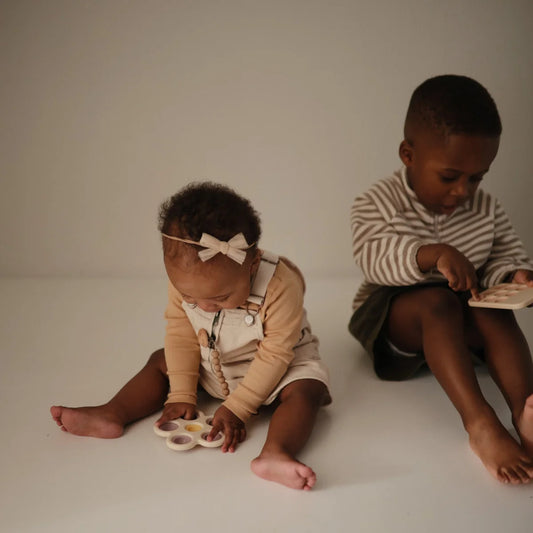 Zwei Kinder spielen mit Blume Plop-it Spielzeug in Lila und Gelb, einer liest ein Buch