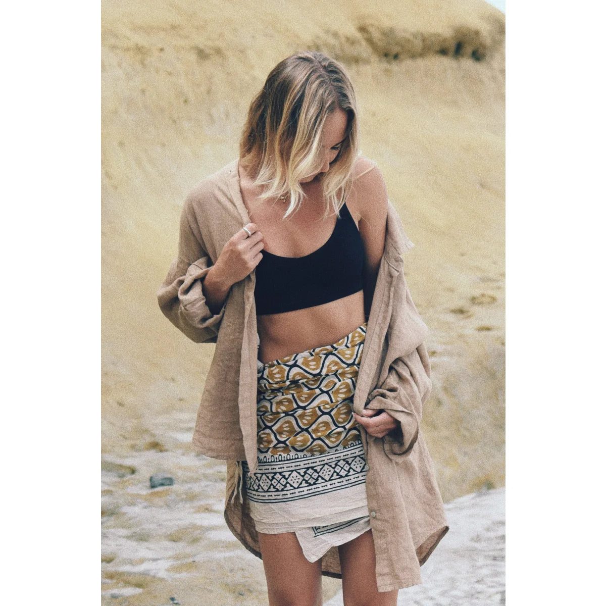 Frau in schwarzem Crop-Top, gemustertem Rock und beigem Cardigan am Strand