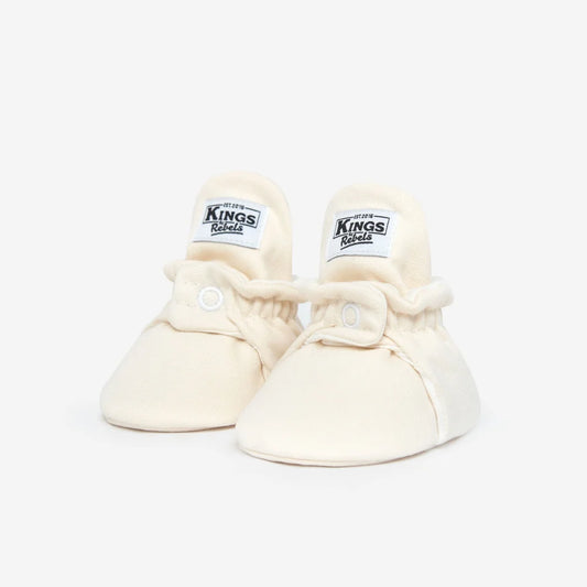 Ein Paar crèmefarbene Babybooties mit Kings-Labeln für 0-12 Monate