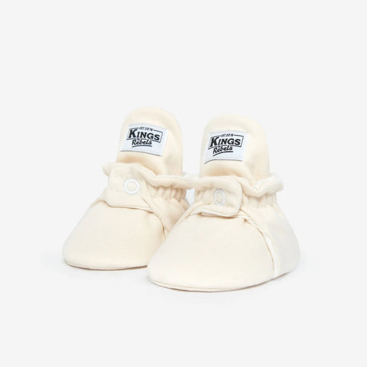 Ein Paar crèmefarbene Babybooties mit Kings-Labeln für 0-12 Monate