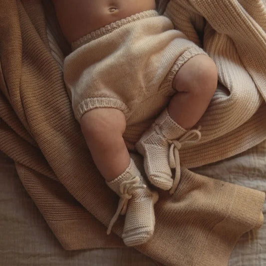 Babylegs in gestrickten Stiefeln auf einer weichen Decke, Creme Booties