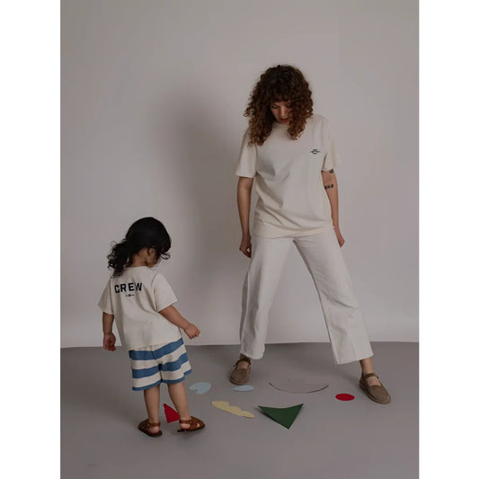 Eine frau trägt ein off white boxy t-shirt mit stickerei und weiten weißen hosen daneben steht ein kind in minimalistischer kleidung