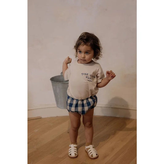 Junger Junge in cremefarbenem Shirt und Karoshorts mit Eimer in der Hand