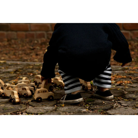 Ein kind in dunkel sweater und gestreifter hose spielt mit hölzernen bus spielzeugautos auf steinweg nachhaltige babykleidung schweiz