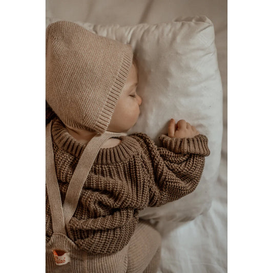 Baby in Chunky Knit Sweater and Bonnet, resting on a soft pillow