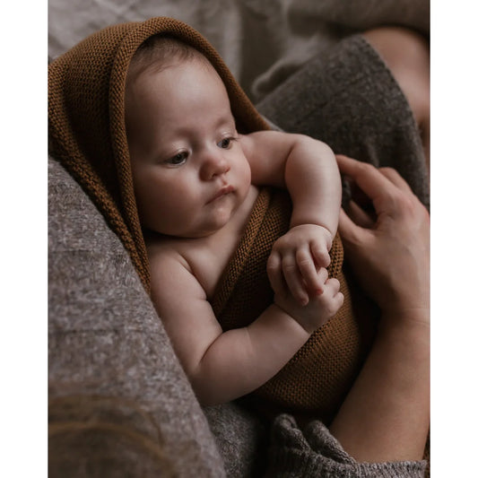 Baby in einer braunen Cocoon Babydecke für zusätzlichen Komfort und ökologische Kinderbekleidung