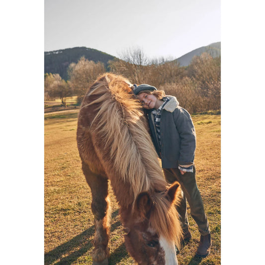 Junge lehnt an einem Pferd, trägt Corduroy-Hosen in Kaki für stilvolle Freizeitmode