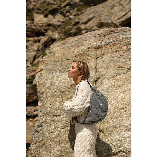 Frau trägt cremefarbenes Kabelstrickkleid und grauen Rucksack mit weißen Herzmustern