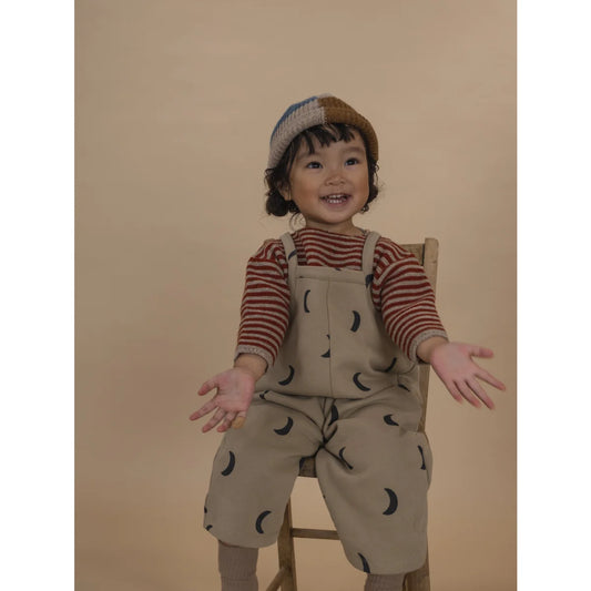 Lächelndes Kind in gestreiftem Hemd, Mond-überzogene Latzhose und Farbblock-Strickmütze