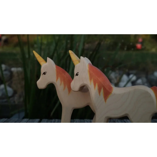 Zwei hölzerne Einhornfiguren mit orangefarbenen Mähnen und Schweifen