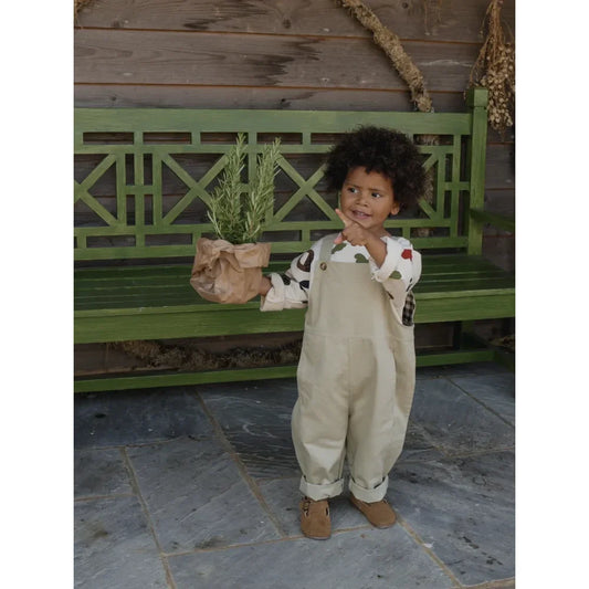 Kind im cremefarbenen Overall hält einen Blumentopf, Farmer Dungarees Latzhose von Seasalt
