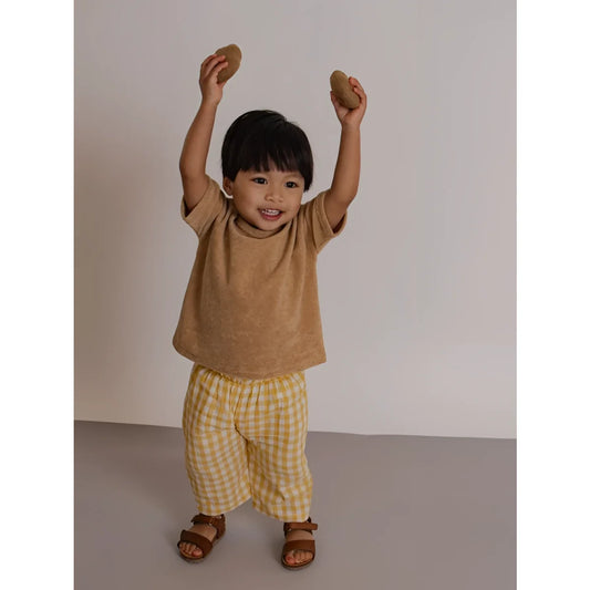 Fröhliches Kleinkind in Fisherman Pants Honeycomb Gingham mit Steinen überm Kopf