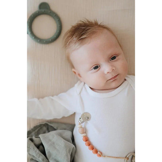 Baby in weißem Overall mit dekorativem Perlenanhänger, Fixleintuch Fog Nebel