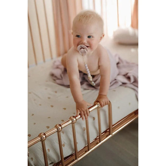 Baby mit blonden Haaren am Gitter eines Betts mit Fixleintuch Rainbow