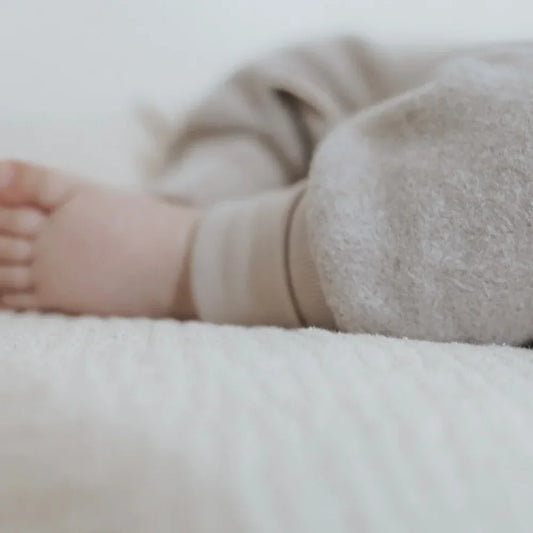 Babyfuß und Bein auf weichem Untergrund in beigen Fleece Pumphosen