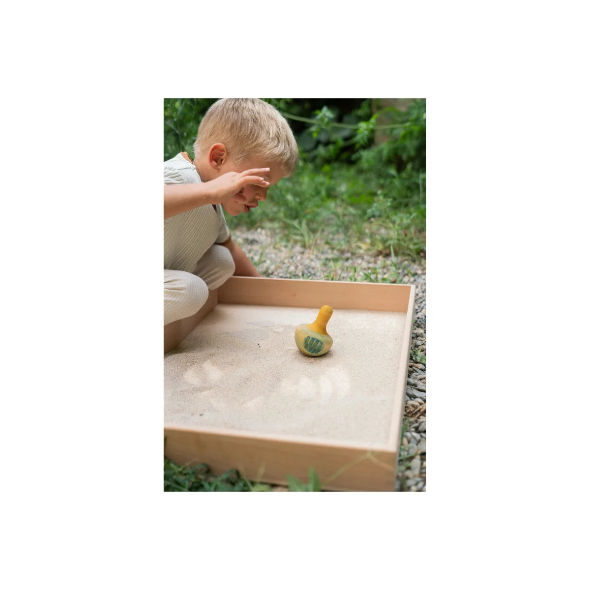 Holz-Sandkasten mit gelbem Spaten und grünem Spielzeugvogel