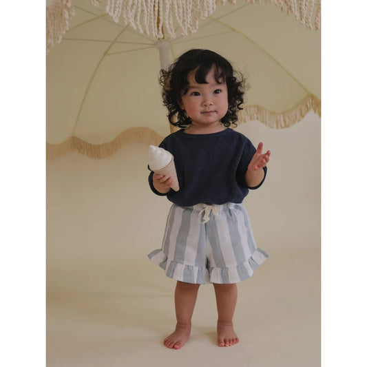 Kleinkind in gestreiften Shorts hält eine Spielzeug-Eiskoniche. Frill Shorts