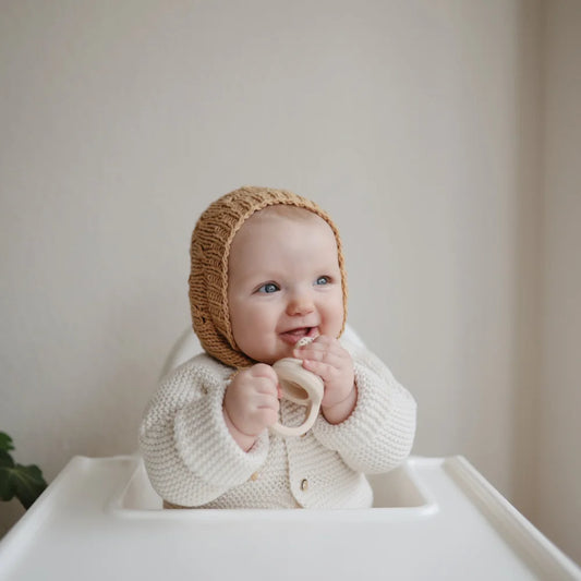 Lächelndes Baby in gestrickter Mütze und weißem Sweater mit Fruchtsauger 2er Set