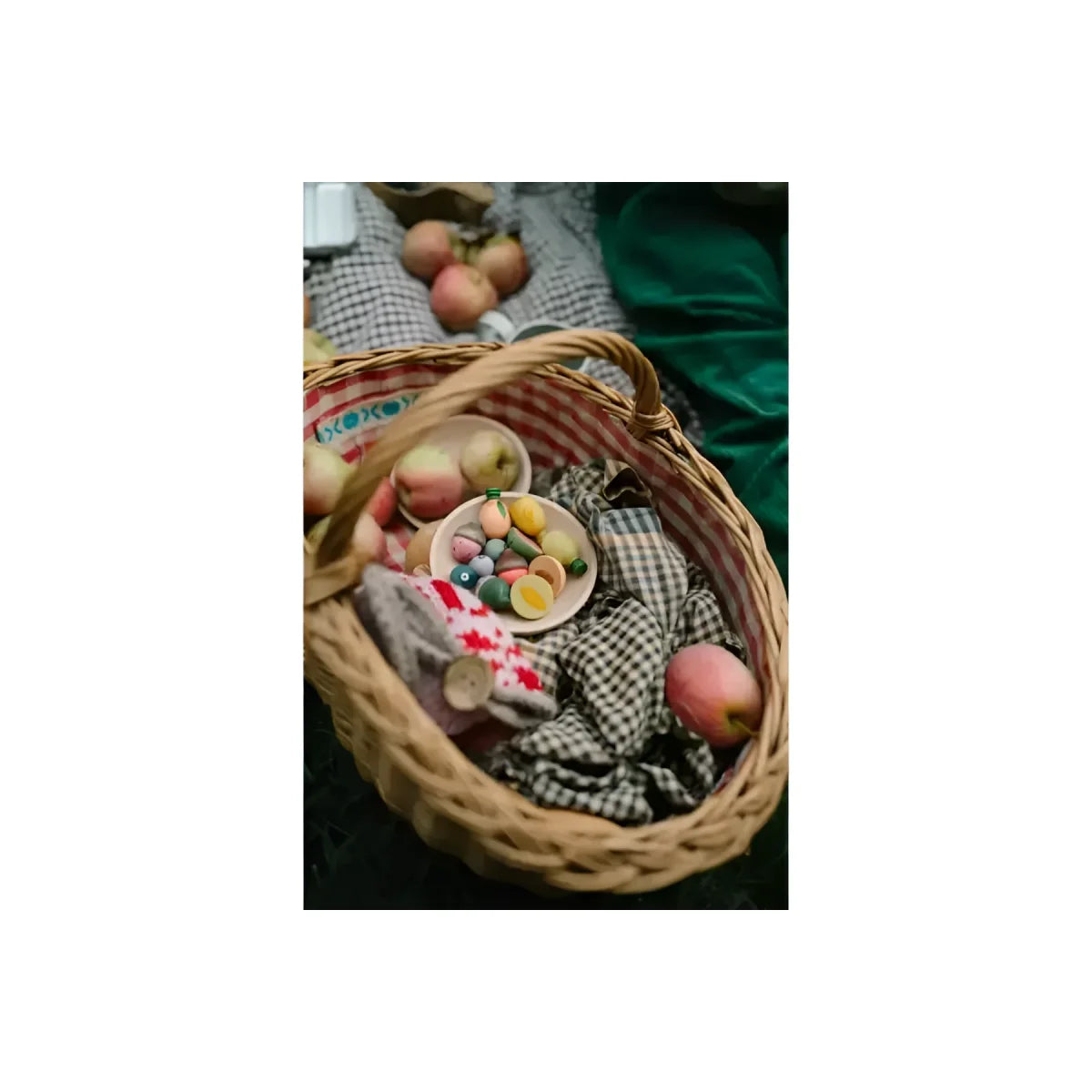 Woven wicker picnic basket with red and white checkered lining holding apples and colorful candies for fruits