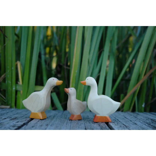 Drei hölzerne Gänsefiguren mit orangefarbenem Schnabel und Füßen
