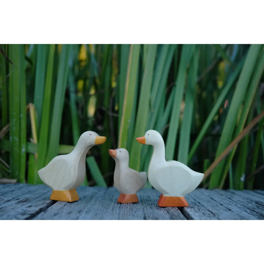 Drei hölzerne Gänsefiguren mit orangefarbenem Schnabel und Füßen