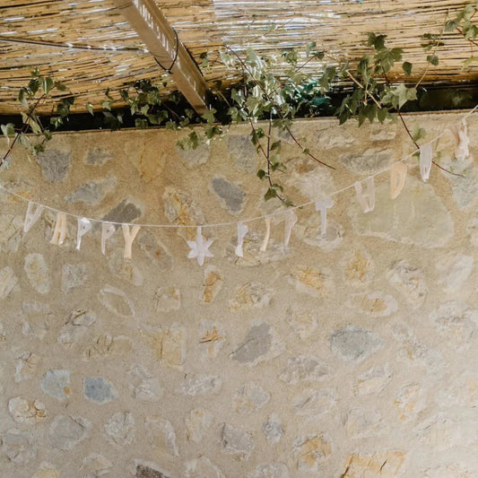 Weisse Leevje Girlande happy birthday in Lavender mit Sternausschnitten über einer Steinmauer