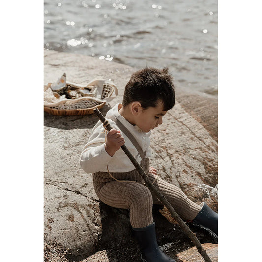 Junger Junge in Vintage-Kleidung sitzt auf Felsen am Wasser neben Granny Teddy Strumpfhosen