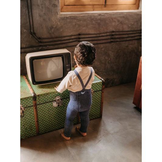 Kind steht vor einem alten Fernseher auf einem Vintage-Koffer in Steel Blue Strumpfhosen